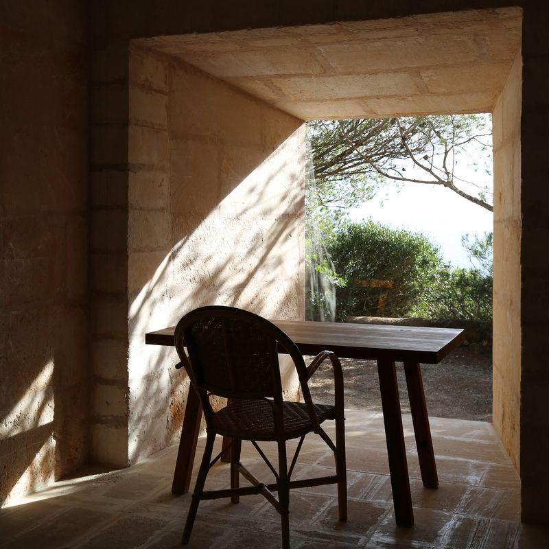 Quiet table and chair in a sunlit stone interior opening onto a garden